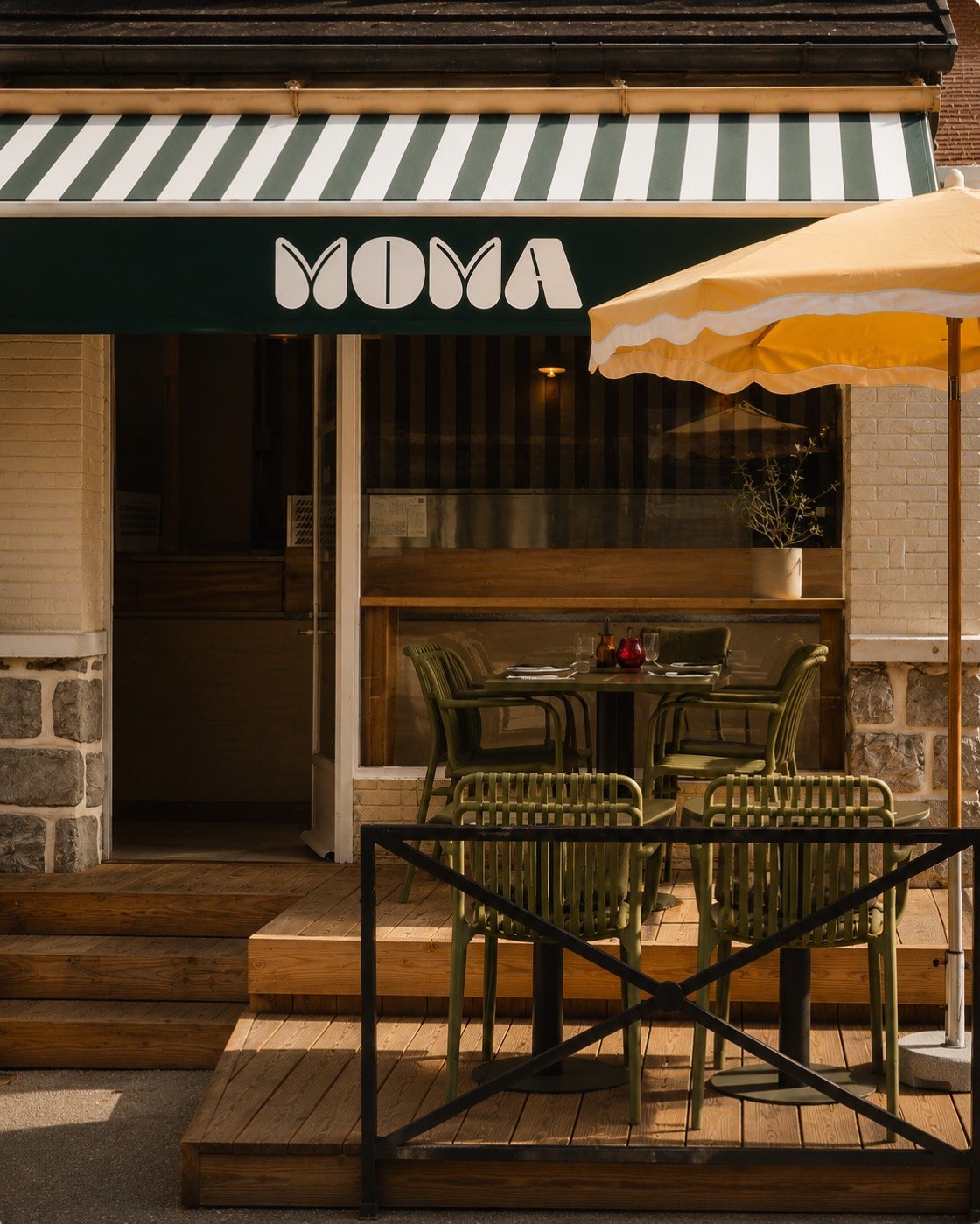 La façade du restaurant MOMA à Veyrier-du-Lac : l’enseigne sur le store banne vert, le parasol ocre et la terrasse en bois.